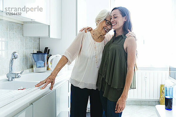 Lächelnde Enkelin und Großmutter  die sich in der Küche zu Hause umarmen