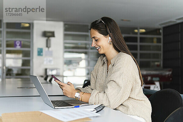 Lächelnde junge Geschäftsfrau mit Smartphone am Schreibtisch im Büro