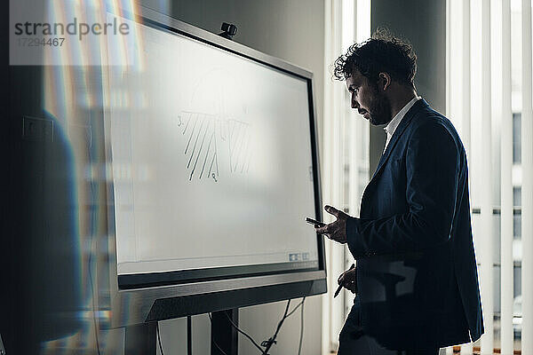 Männlicher Unternehmer betrachtet ein Diagramm auf einer Projektionsfläche im Büro