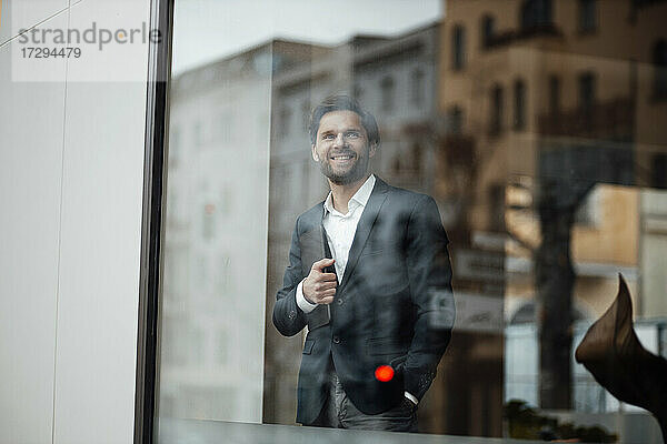 Männlicher Unternehmer  der ein digitales Tablet hält  während er am Bürofenster steht
