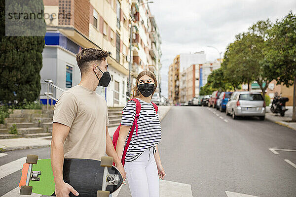 Ehepaar mit Gesichtsschutz beim Überqueren der Straße in der Stadt während des COVID-19-Ausbruchs