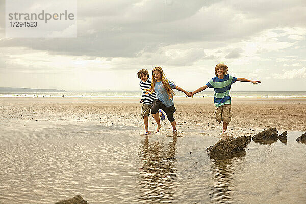 Glückliche Freunde halten sich beim Laufen am Strand an den Händen