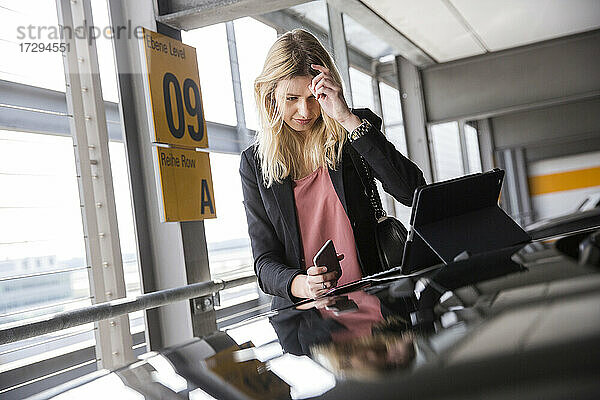 Junge Frau schaut auf einem Parkplatz auf ein digitales Tablet