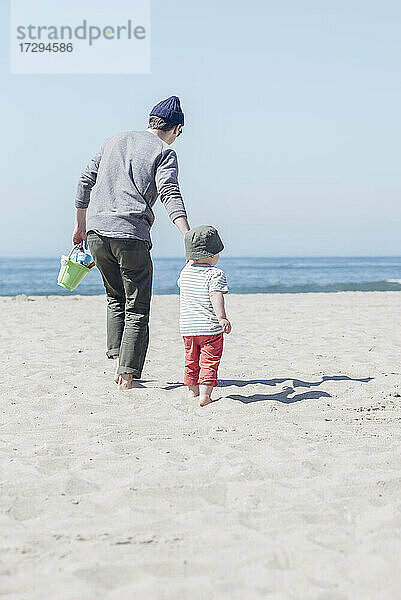 Sohn geht mit Vater am Strand spazieren und hält sich an den Händen