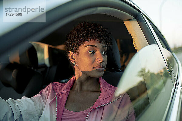 Junge Frau schaut im Auto sitzend vom Fenster weg