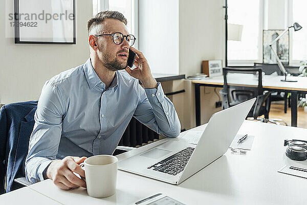 Geschäftsmann  der am Arbeitsplatz sitzend mit seinem Mobiltelefon telefoniert