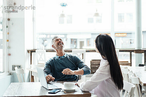 Lächelnder Geschäftsmann schaut auf eine Drohne  während er mit einem Kollegen im Café sitzt