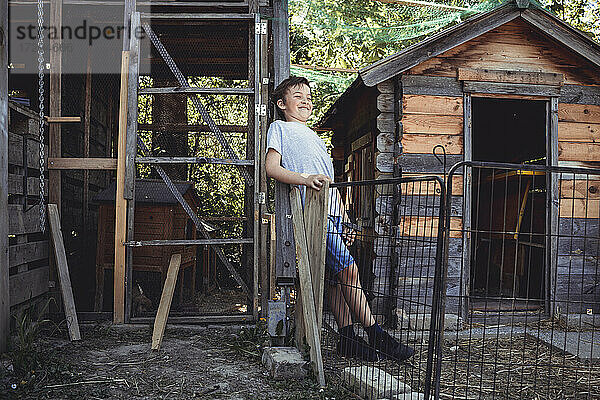 Lächelnder Junge  der neben einem Kaninchenstall im Hinterhof steht