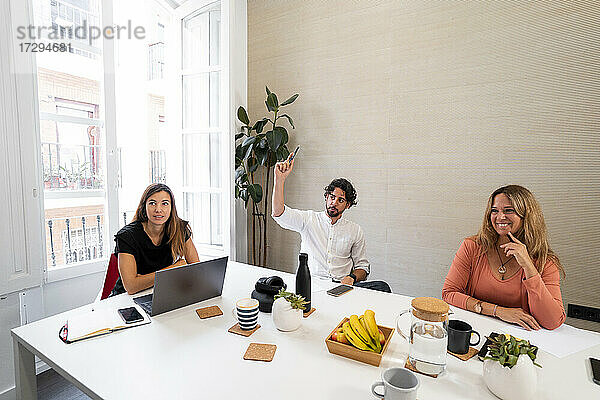 Männlicher Unternehmer hebt die Hand während eines Treffens im Coworking-Büro