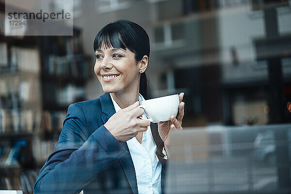 Lächelnde Besitzerin mit Kaffeetasse  die in einem Café wegschaut