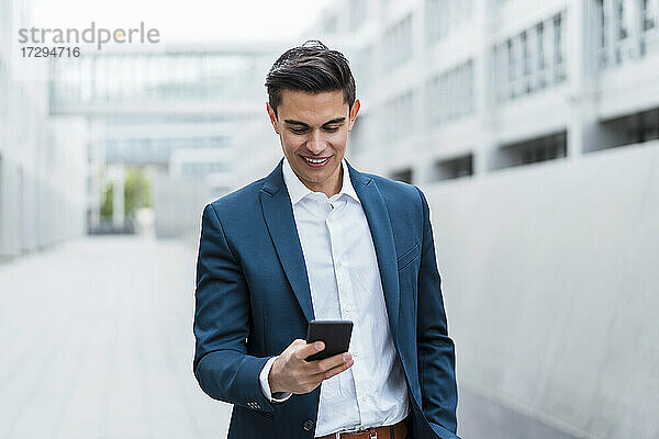 Lächelnder männlicher Berufstätiger  der im Freien stehend eine Textnachricht über sein Smartphone verschickt