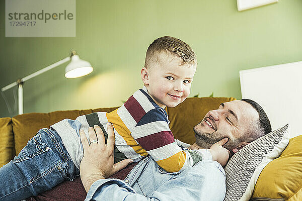 Niedlicher Junge liegt mit seinem Vater auf dem Sofa im Wohnzimmer zu Hause