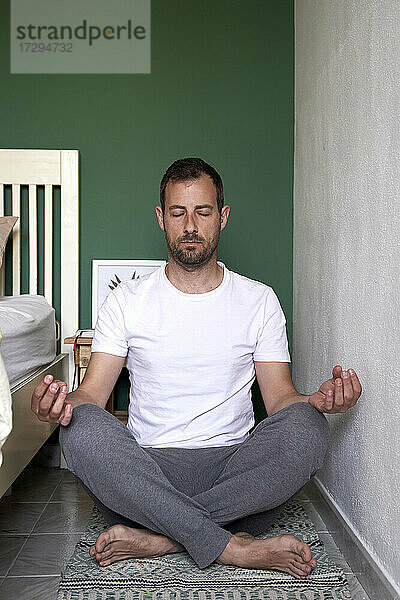 Mittlerer erwachsener Mann  der im Schlafzimmer sitzend Yoga praktiziert