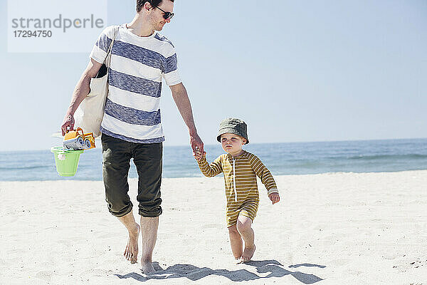 Junge mit Hut geht mit seinem Vater am Strand spazieren