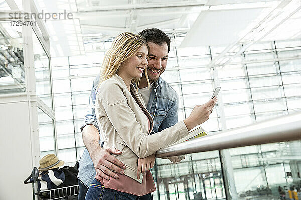 Junges Paar schaut im Abflugbereich eines Flughafens auf sein Smartphone