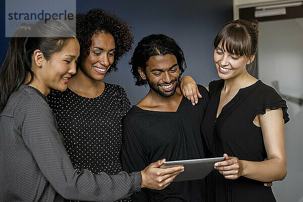 Lächelnder männlicher und weiblicher Unternehmer  die sich ein digitales Tablet teilen  während sie sich im Büro unterhalten