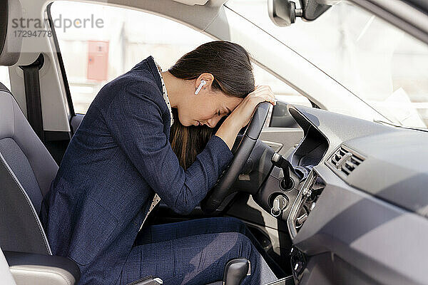 Müde Geschäftsfrau  die ihren Kopf im Auto auf das Lenkrad legt