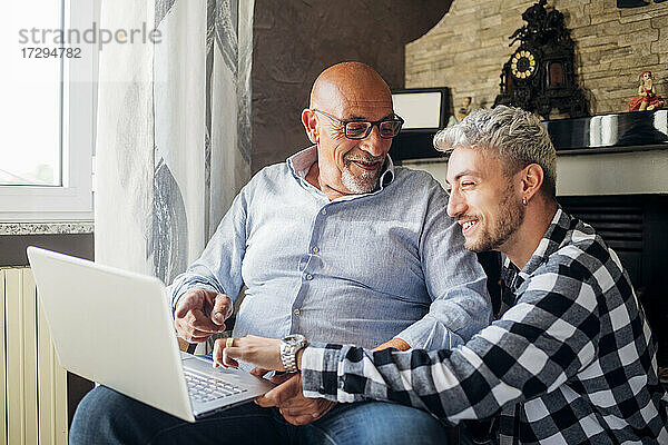 Lächelnder Vater und Sohn teilen sich einen Laptop  während sie zusammen zu Hause sitzen