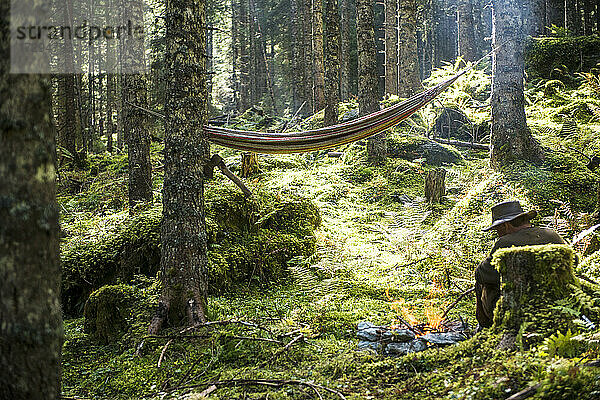 Mann entspannt sich vor einem Lagerfeuer aus Stein  das im Wald brennt