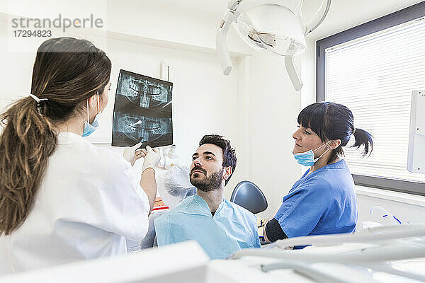 Zahnärztin mit Assistentin  die einem Patienten in einer medizinischen Klinik eine Röntgenaufnahme erklärt