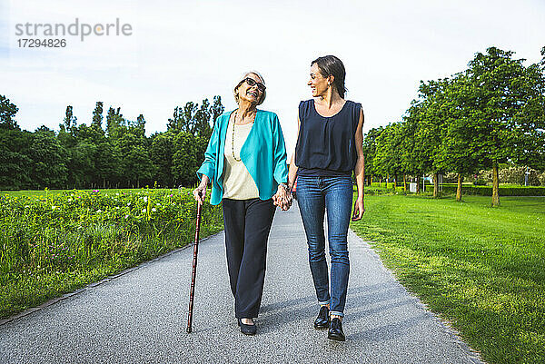 Lächelnde Großmutter hält die Hand ihrer Enkelin beim Spaziergang auf der Straße