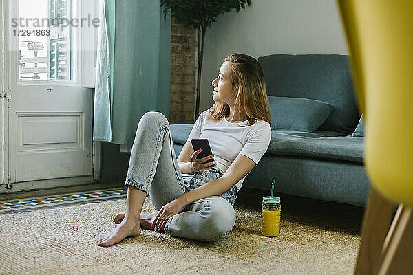 Junge Frau schaut weg  während sie zu Hause auf dem Teppich sitzt
