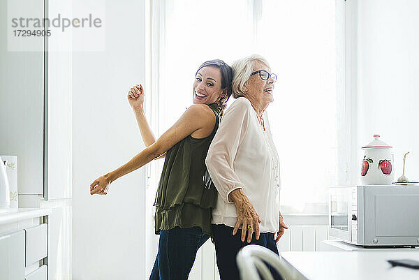 Lächelnde ältere Frau tanzt mit Enkelin in der Küche zu Hause