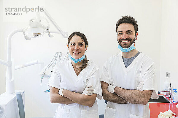 Lächelnde Zahnärztinnen und Zahnärzte stehen mit verschränkten Armen in einer medizinischen Klinik