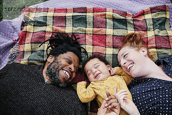 Glückliche Familie spielt mit niedlichen Sohn  während auf Picknickdecke im Park liegen