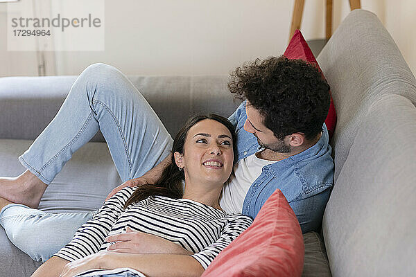 Lächelnde Freundin schaut ihren Freund an  während sie zu Hause auf dem Sofa liegt