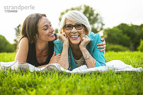 Lächelnde Enkelin mit Arm um die Großmutter  die auf einer Picknickdecke ruht