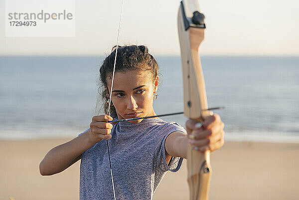Junge Frau übt Bogenschießen am Strand