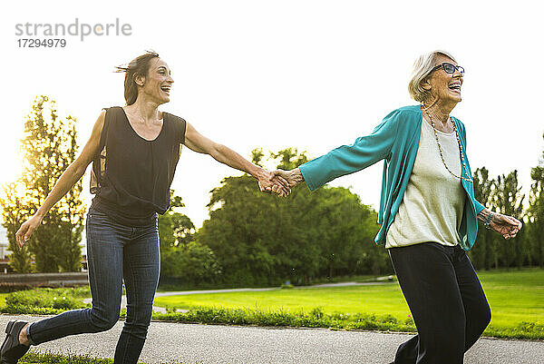 Verspielte Großmutter hält die Hand ihrer Enkelin beim Laufen im Park