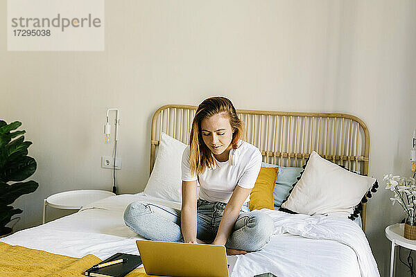 Junge Frau benutzt einen Laptop  während sie zu Hause auf dem Bett sitzt
