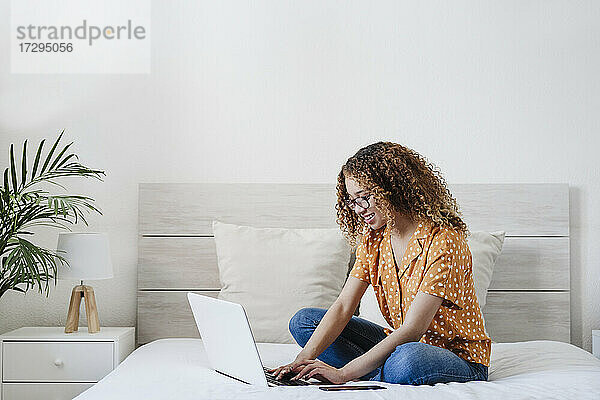 Lächelnde junge Frau mit Laptop auf dem Bett zu Hause