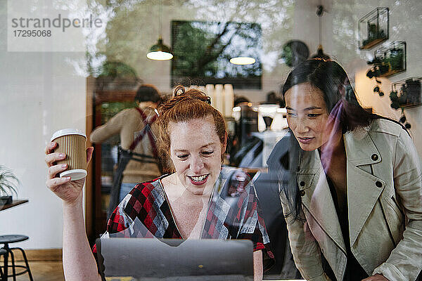 Frau mit Einweg-Kaffeebecher benutzt Laptop von Freundin in Café