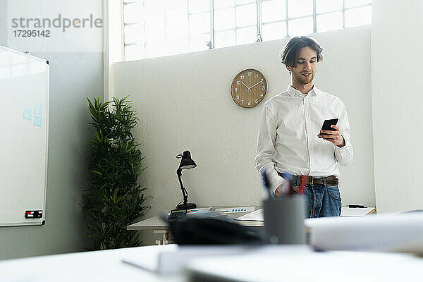 Geschäftsmann  der ein Mobiltelefon benutzt  während er in einem kreativen Büro steht