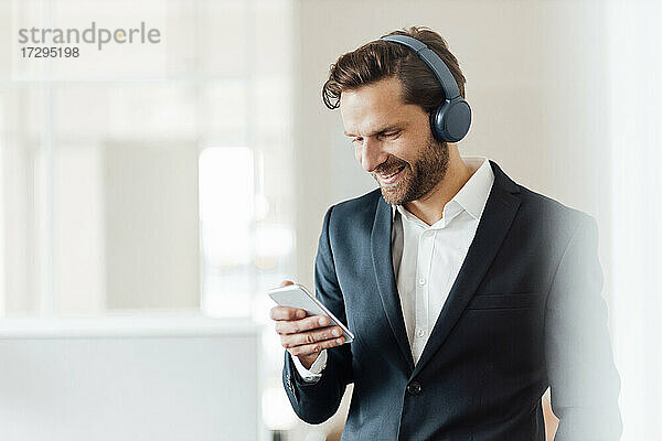 Männlicher Unternehmer mit Kopfhörern und Smartphone im Büro