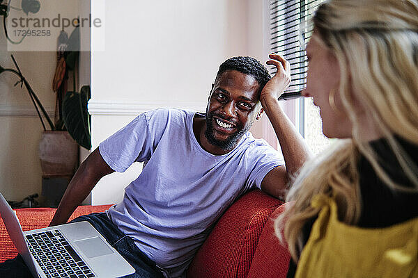 Lächelnder Mann mit Laptop  der eine Frau auf dem Sofa sitzend betrachtet