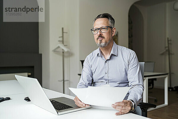 Geschäftsmann mit Laptop und Papierkram bei der Arbeit am Schreibtisch