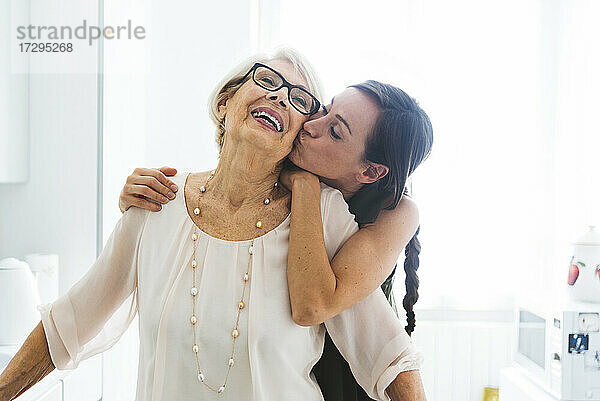Mid erwachsene Frau mit Arm um küssen Großmutter Wange zu Hause
