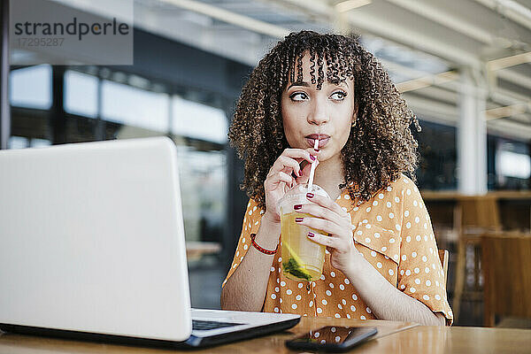 Junge Geschäftsfrau schaut weg  während sie in einem Café Eistee trinkt