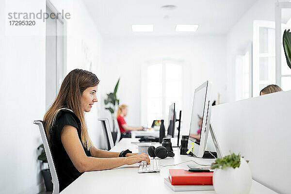 Geschäftsfrau arbeitet an einem Desktop-Computer  während sie in einem Coworking-Büro sitzt
