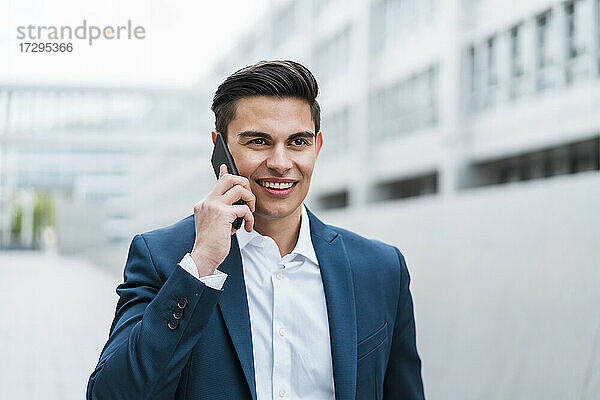 Lächelnder Geschäftsmann  der im Freien stehend mit seinem Mobiltelefon spricht