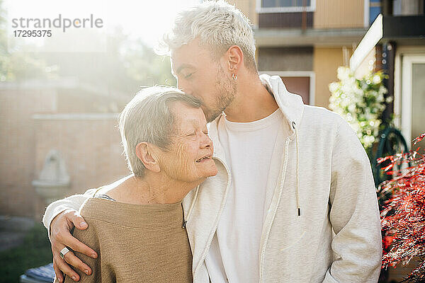Junger Mann küsst Großmutter auf die Stirn  während er im Hinterhof steht und den Arm um sie legt