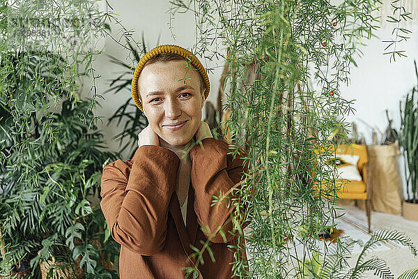 Lächelnde Geschäftsfrau mit Strickmütze bei Pflanzen im grünen Büro