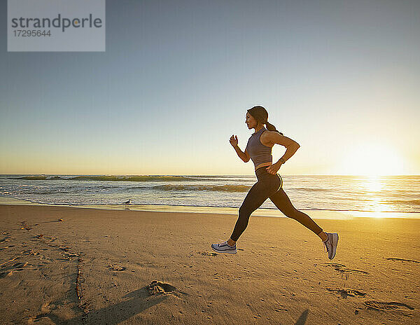 Frau joggt am Strand bei Sonnenuntergang