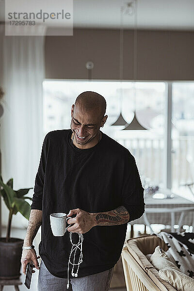 Hispanic Mann lachend  während hält Kaffeebecher im Wohnzimmer