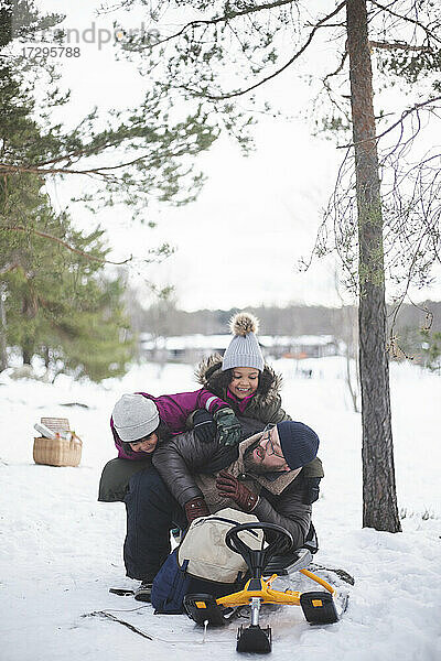 Fröhliche Mädchen spielen mit Vater auf Schnee während der Ferien