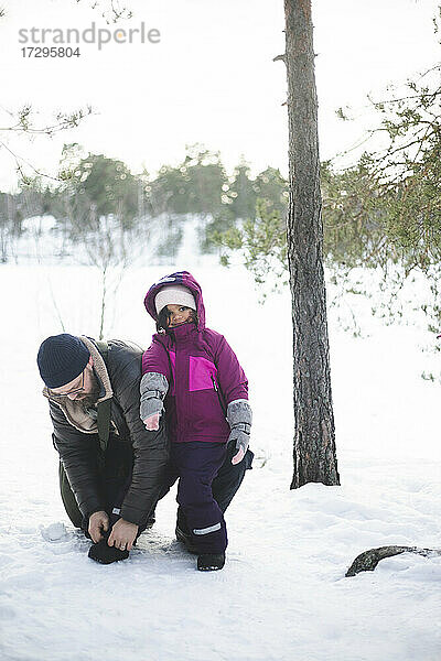 Reifer Mann hilft Tochter mit Schuh auf Schnee